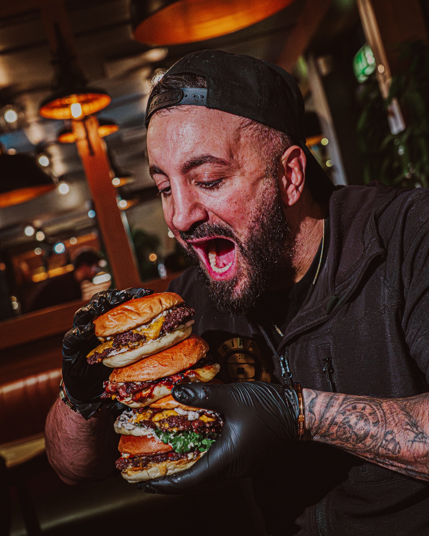 Grundaren i bakåtvänd keps tar sig an ett torn av fyra staplade smashburgare